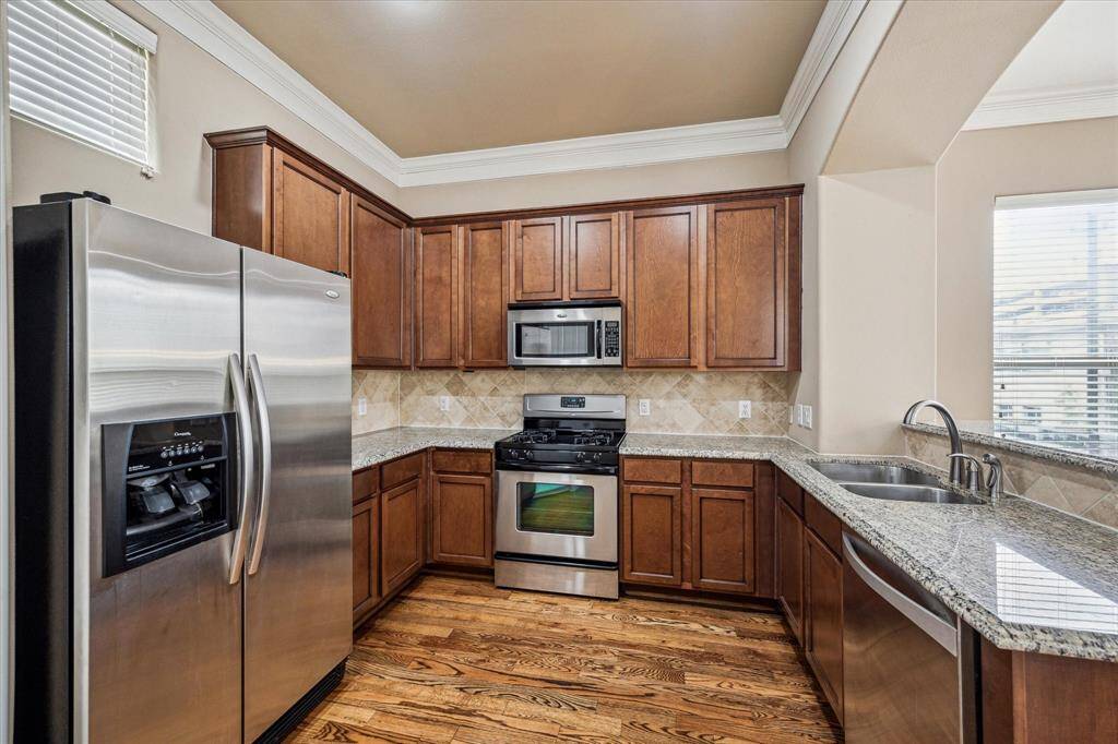 The kitchen boasts stainless steel appliances, granite countertops, a travertine backsplash, bar-top seating, and warm wood floors—all combining to create a timeless look that can lean classic or modern depending on your décor. Open to the main living area, this versatile space is perfect for entertaining, holiday gatherings, and inclusive living.