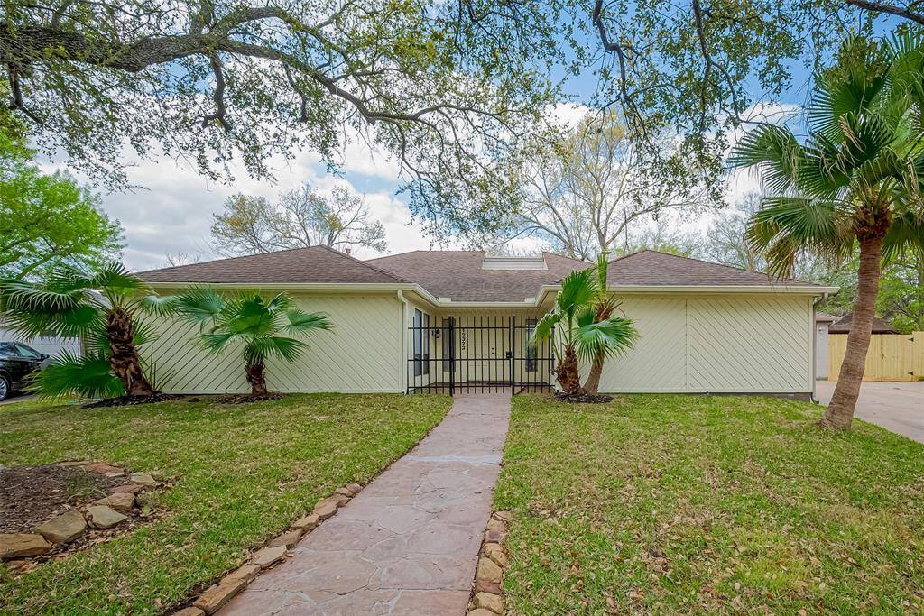 Charming single-story home with a well-maintained lawn, mature trees, and palm plants. Features a welcoming path leading to a gated entry. Perfect for those seeking a cozy and serene setting.