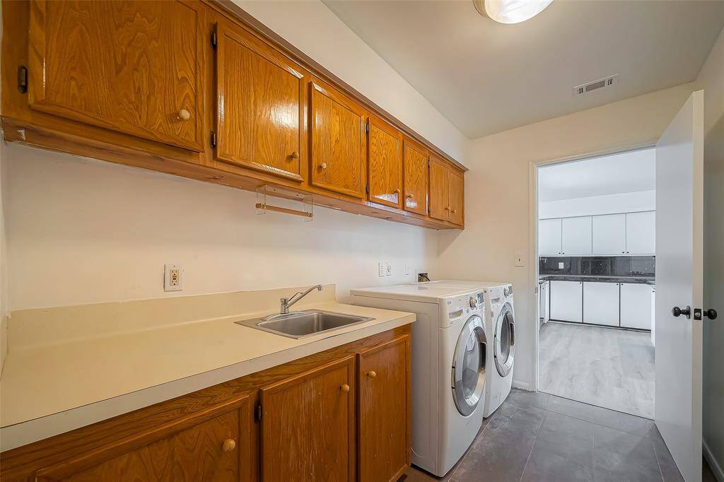 This photo showcases a functional laundry room with wooden cabinets, a countertop and sink, and space for a washer and dryer.