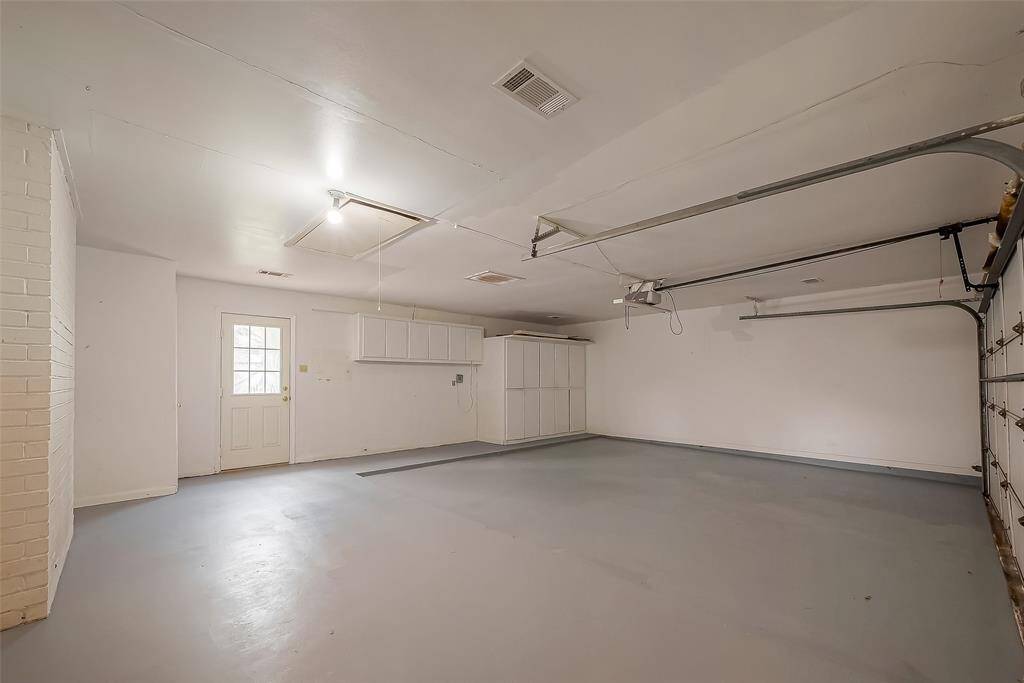 This is a spacious, clean garage with a painted floor, overhead storage, and a side door for easy access. Ideal for parking and additional storage.