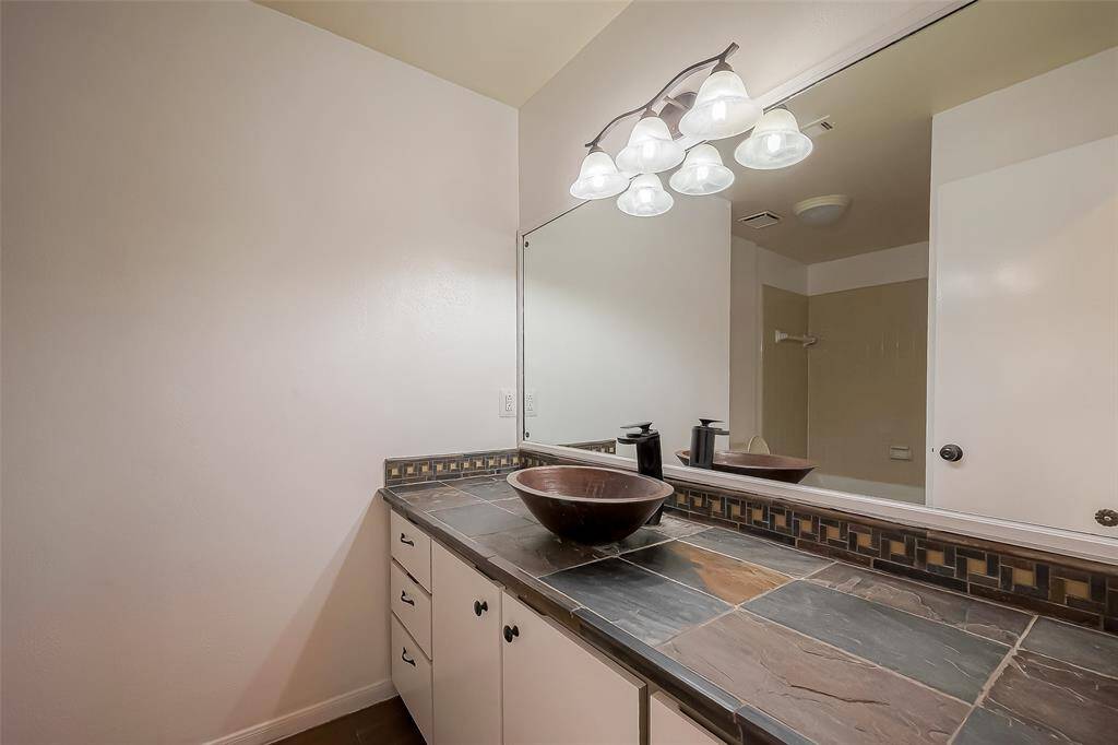 This bathroom features a sleek design with a large mirror, elegant lighting, and a unique stone countertop with a vessel sink.