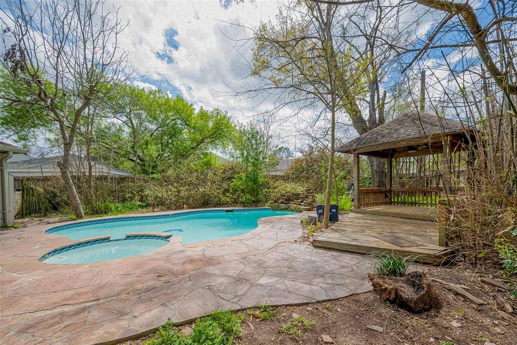 This backyard features a serene pool with a natural stone patio and a cozy wooden gazebo, perfect for relaxation and entertaining amidst lush greenery.