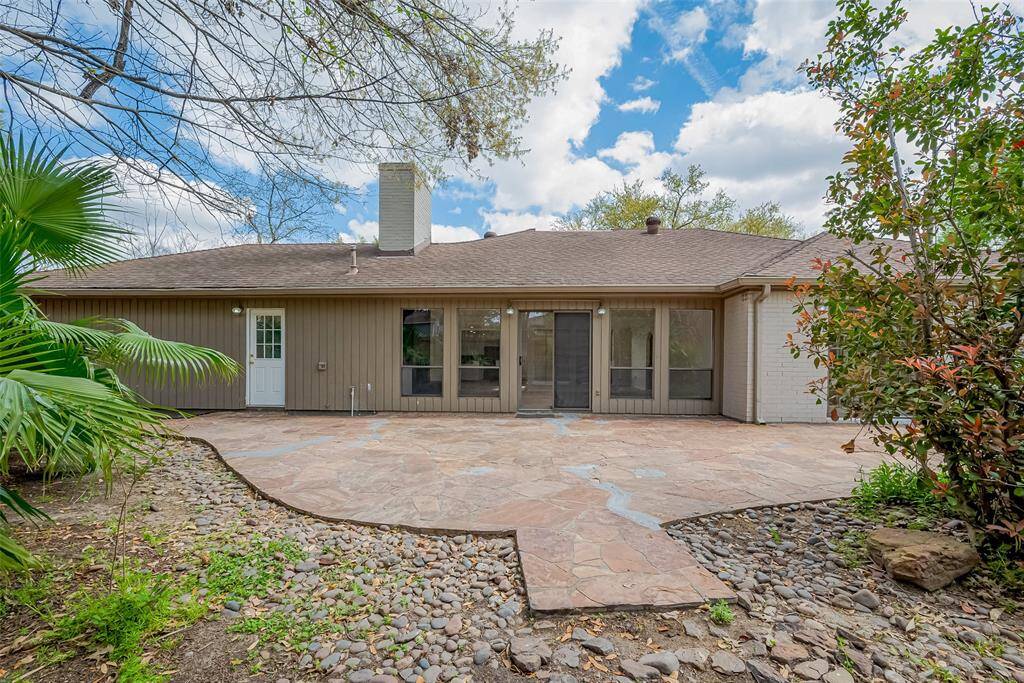 This photo showcases a charming home's backyard featuring a spacious stone patio, perfect for outdoor gatherings. The exterior has a natural wood finish with large windows, and the surrounding greenery adds to the serene atmosphere.