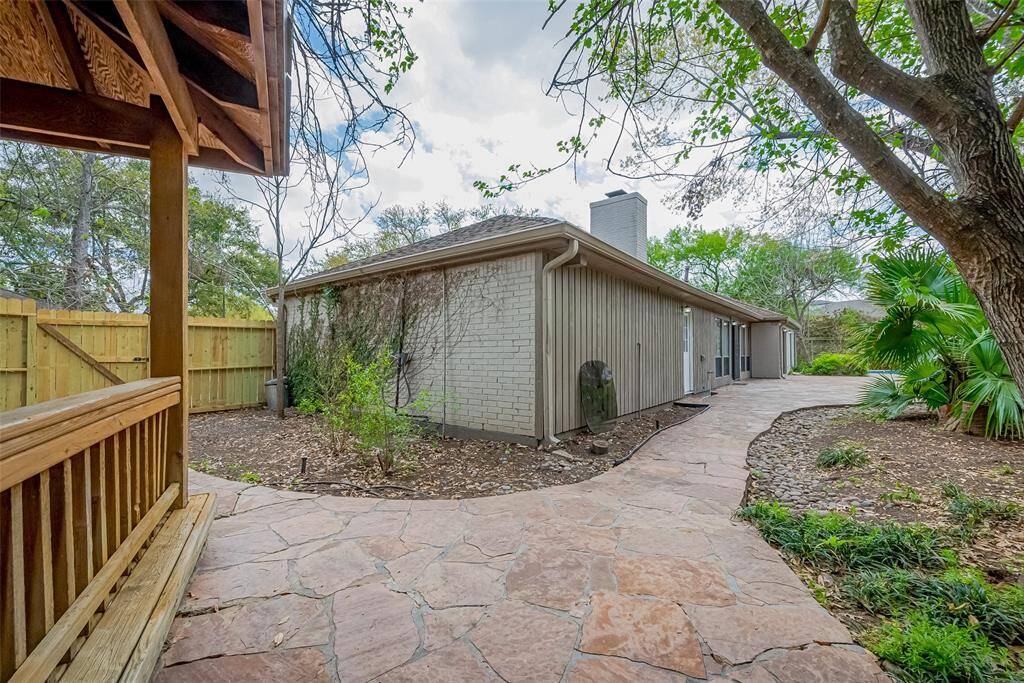 This photo showcases a charming backyard with a stone pathway leading to a single-story home. The yard features mature trees, a wooden fence, and a small patio area, creating a natural and inviting outdoor space.