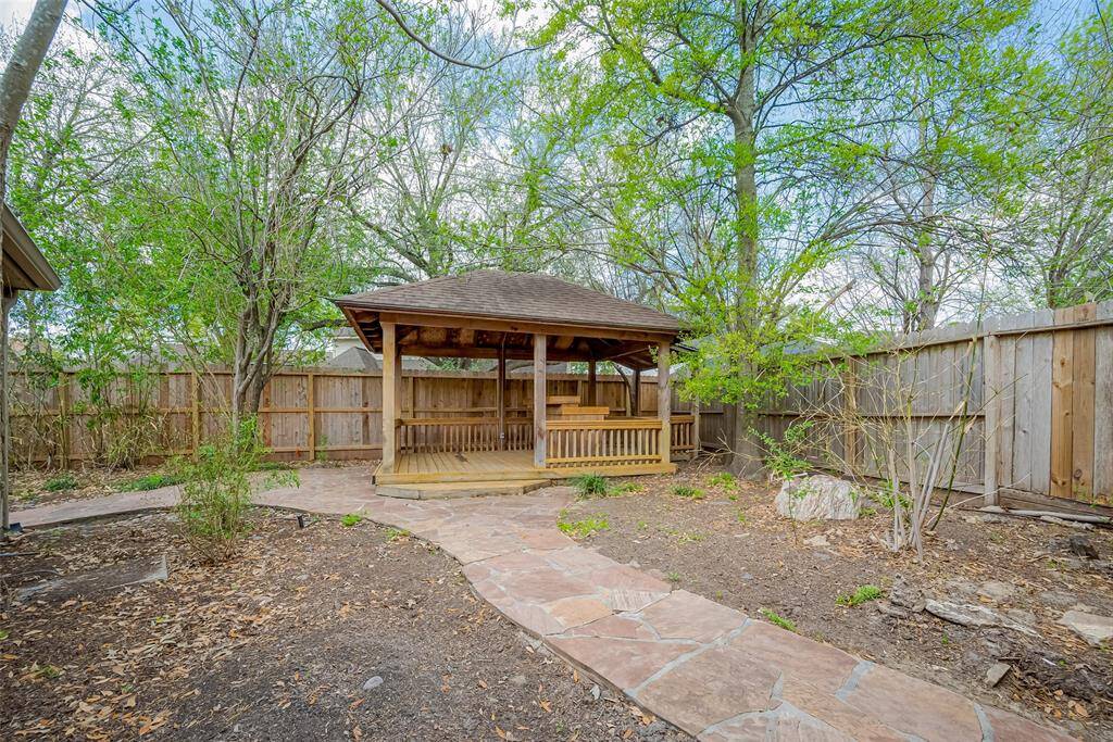 Charming backyard features a wooden gazebo surrounded by mature trees and a privacy fence, with a stone pathway leading up to it—perfect for outdoor relaxation and entertaining.