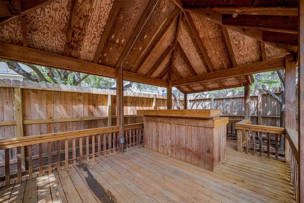This photo showcases a charming wooden gazebo with a pitched roof, featuring a built-in bar area and surrounded by a wooden fence, perfect for outdoor entertaining in a private setting.