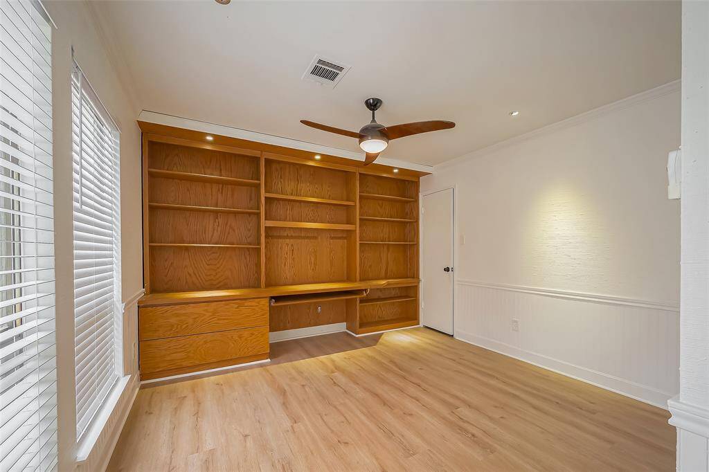 Bright, cozy room featuring built-in wooden shelving and desk, ceiling fan, and large windows with blinds. Ideal for a home office or study.