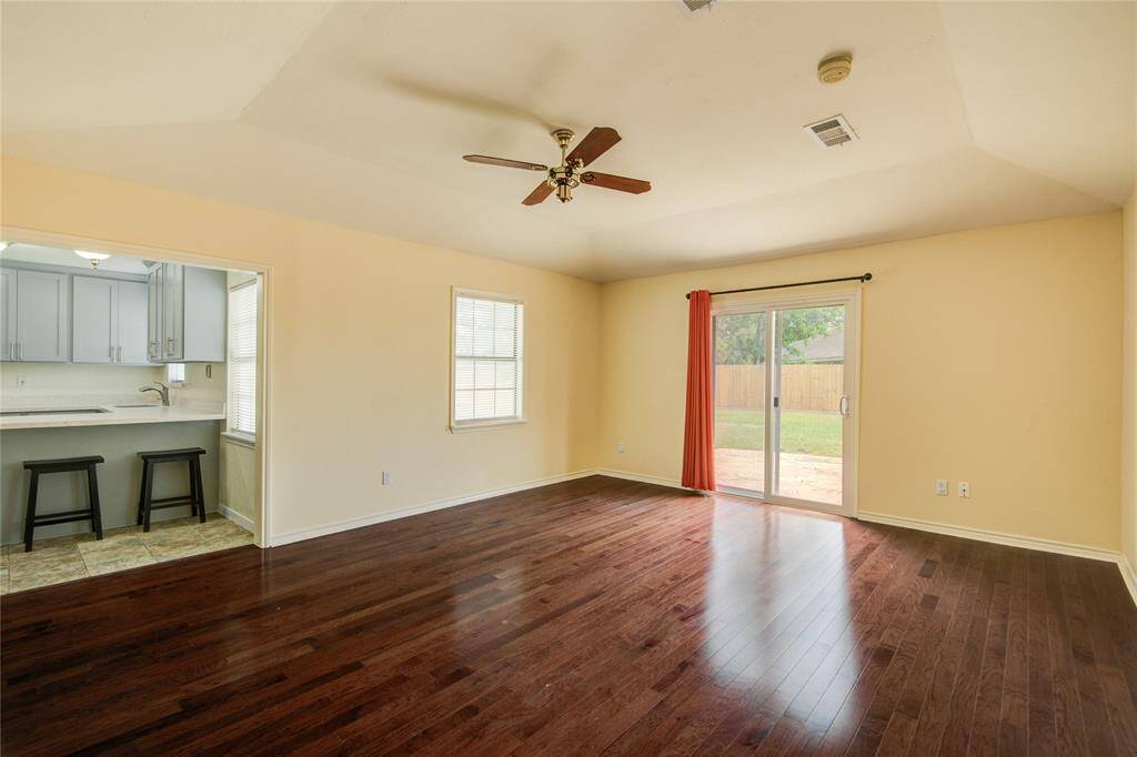 Bright and open family room with rich wood-look flooring, backyard access, and a peek into the adjacent kitchen.
