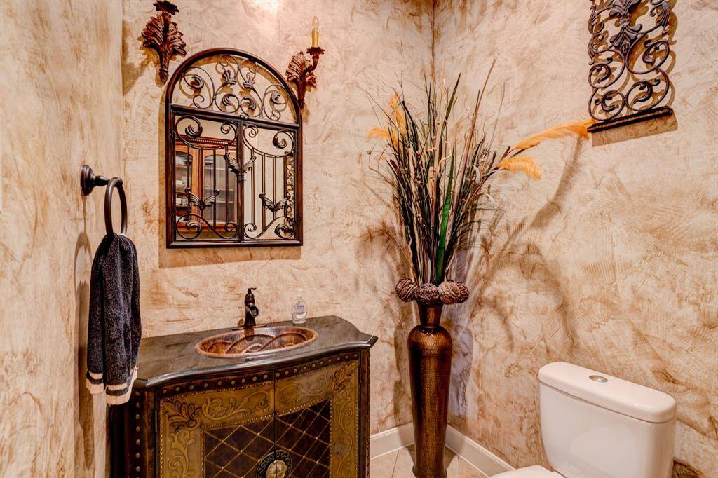 Fashioned to reflect the Mediterranean style, the guest bath features a mirror with iron detailing, textured walls, and a richly patterned storage vanity.
