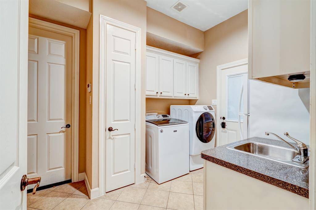 Impressively outfitted, the laundry room has storage cabinetry, a closet, an extra refrigerator, and a sink.