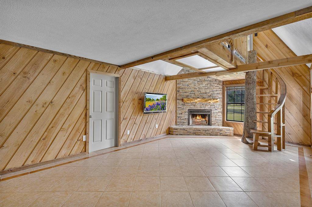 This warm and welcoming space features a stunning cedar accent wall that adds rich texture and a cozy ambiance. At its heart is a floor-to-ceiling stacked stone wood-burning fireplace, perfect for gathering on chilly evenings. The true showstopper? A spiral staircase artfully wrapped around a real tree trunk, blending indoor living with nature in a striking architectural statement.