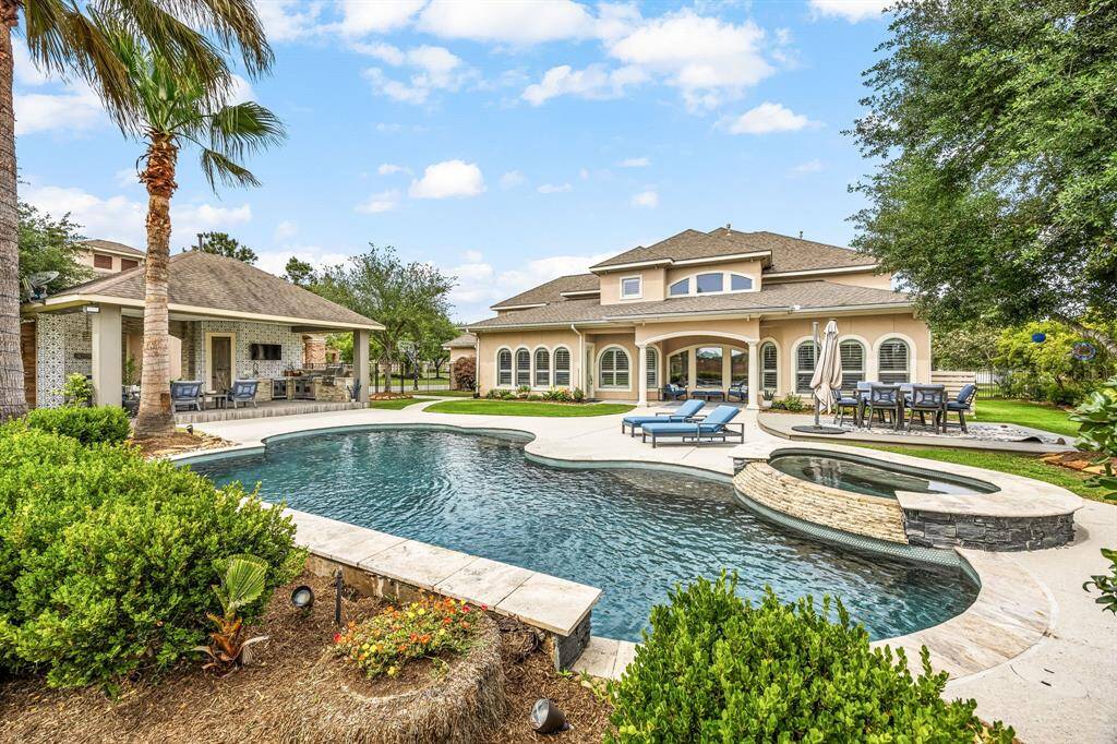 The large yard features outdoor fireplace, patio deck, covered patio, pool and hot tub, dog run and beautiful palm trees