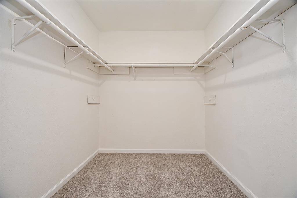 This is a spacious walk-in closet with neutral carpet and white walls, featuring multiple hanging rods for ample storage.