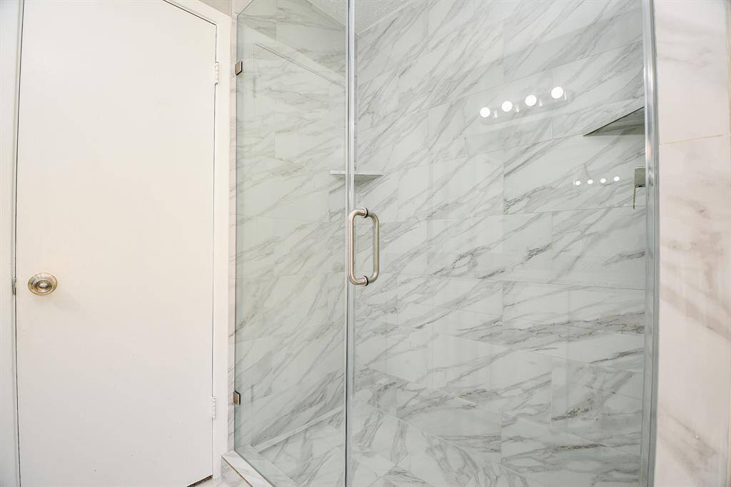 This photo showcases a modern bathroom with a sleek glass shower enclosure featuring elegant marble-patterned tiles. The space appears bright and clean, offering a luxurious feel.