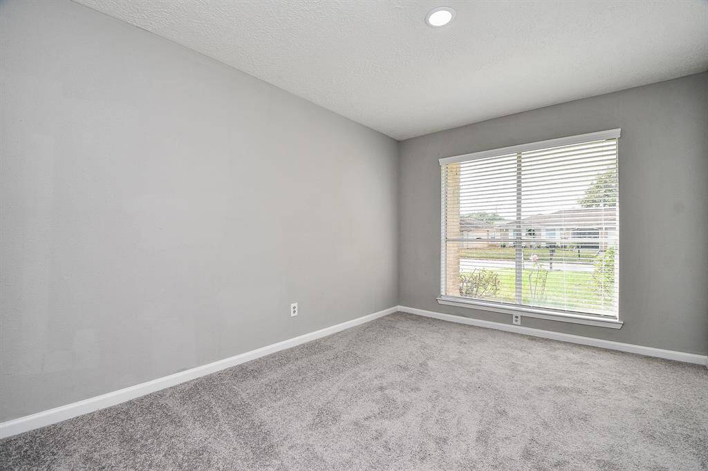 This room features neutral gray walls and carpet, with a large window providing plenty of natural light and a view of the outdoors. Ideal for a cozy living space or office.