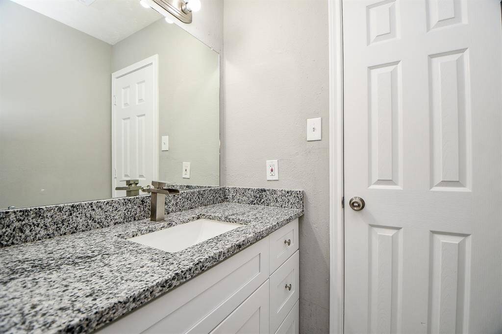 This photo showcases a modern bathroom with a granite countertop, sleek faucet, and white cabinetry. The space features a large mirror and neutral wall color, offering a clean and contemporary feel.