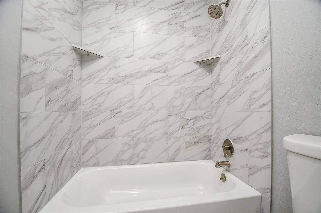 This bathroom features a modern shower-tub combo with elegant white and gray marble-style tiles, equipped with a sleek showerhead and built-in corner shelves.