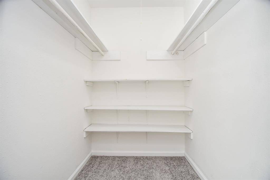 This photo shows a spacious walk-in closet with two hanging rods and three shelves, set against clean white walls and carpeted flooring. Ideal for ample storage and organization.