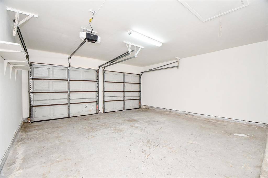 This photo shows a spacious, clean two-car garage with dual automatic doors, white walls, and overhead lighting, ideal for storage or parking.