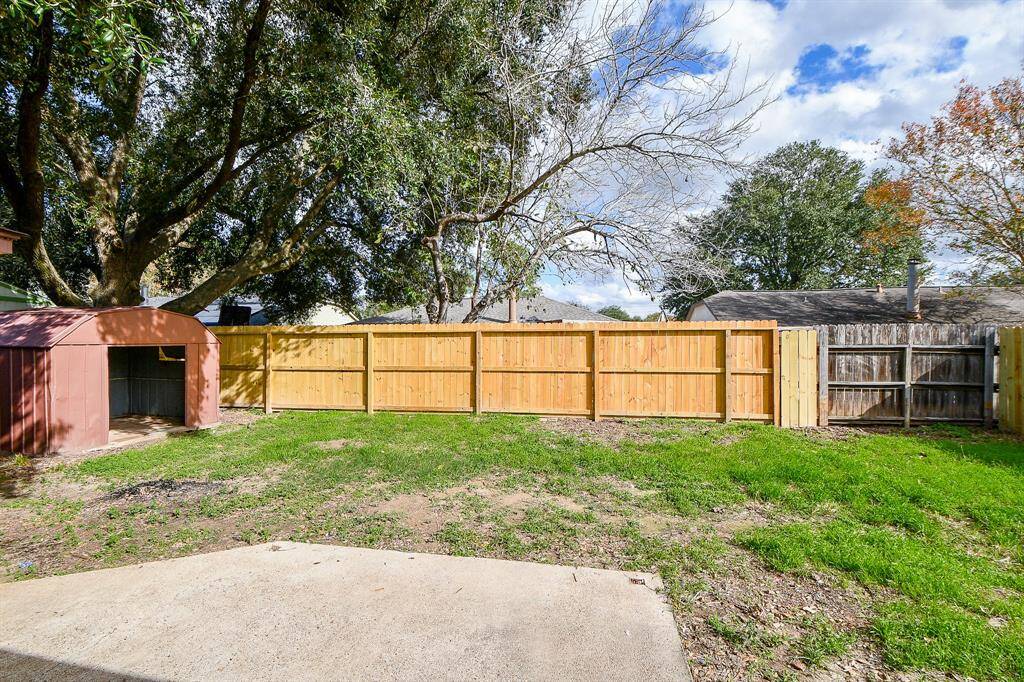 This backyard features a spacious, grassy area with mature trees providing shade. A wooden fence ensures privacy, and there’s a small shed for storage. Ideal for outdoor activities and relaxation.