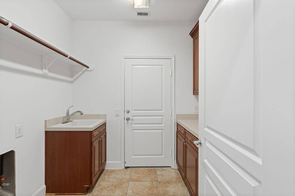 The spacious laundry room is equipped with a sink and ample cabinetry, providing plenty of storage and organization space for all your needs.