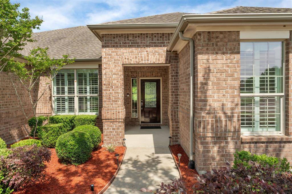 Lush, manicured landscaping frames the walkway to the inviting front porch, where a half-light door gently welcomes natural light into the cheerful entryway.