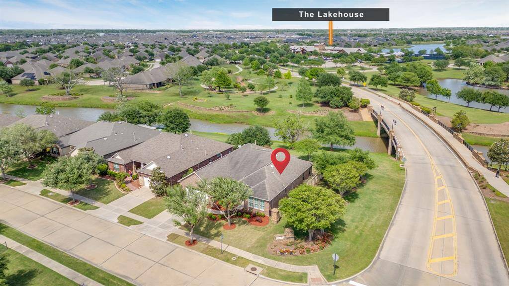 Behind the home, Rabbs Bayou stretches out, framed by lush trees and green space. The Del Webb Bridge offers a scenic view, with the nature park, Lakehouse, and amenities center visible just beyond on the right.