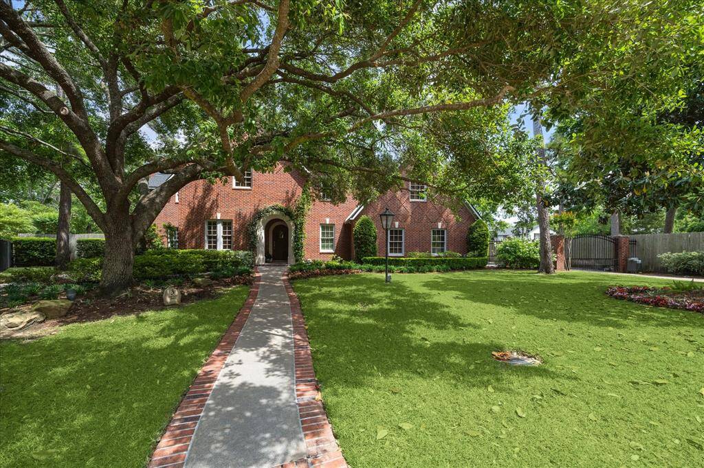 Classic landscaping lead to an arched stone entry, framed by mature magnolias and blooming beds
