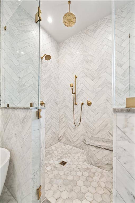 Walk-in shower with herringbone marble tile, dual showerheads, bench seating, and brass finishes—every detail thoughtfully designed.