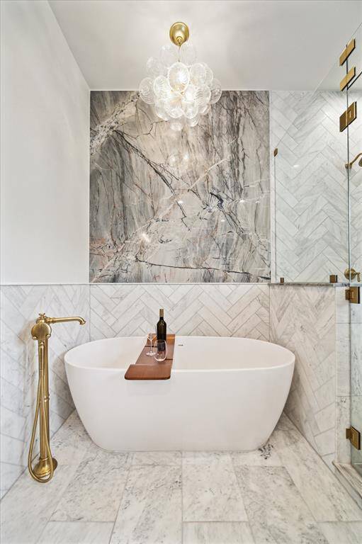 Statement-making slab backsplash brings drama and texture to the serene soaking area, framed by rich gold plumbing and modern lighting