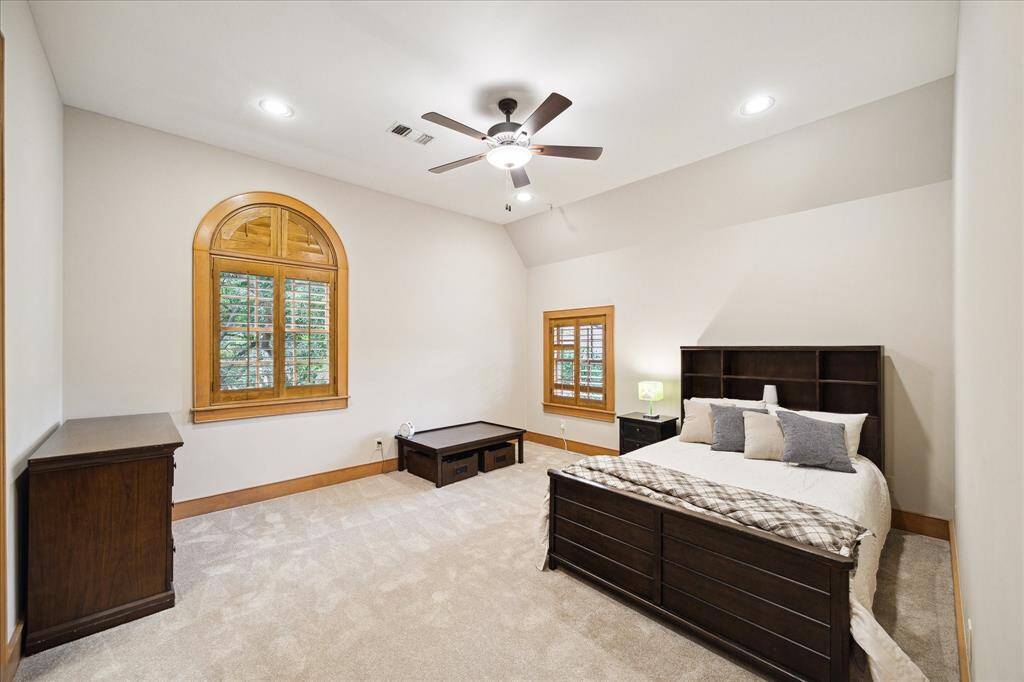 Spacious upstairs bedroom with vaulted ceiling, warm wood trim, and serene views of the treetops through the arched window.