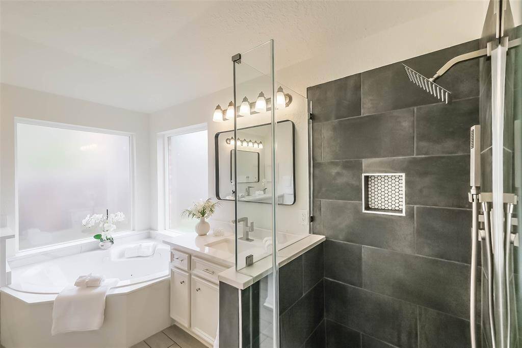 Renovated primary bath has new shower with tile surround, seamless glass door and rainfall shower head with hand held spray wand.