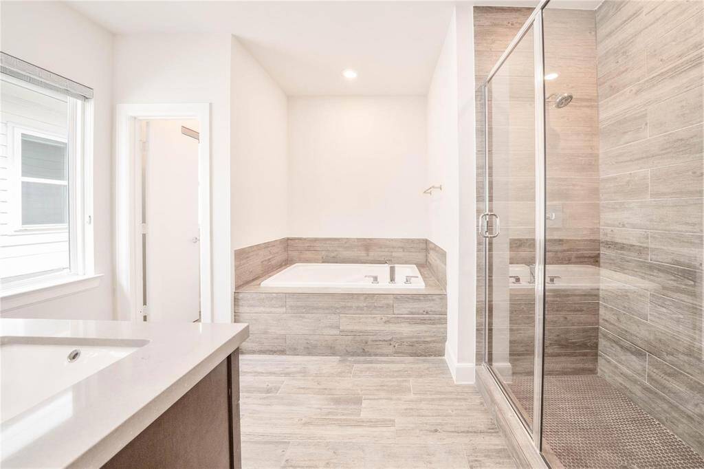 The primary bathroom offers a spacious shower and a soothing jetted tub, complemented by natural tones and modern finishes. It’s a space designed for comfort and relaxation, providing the perfect setting to unwind.