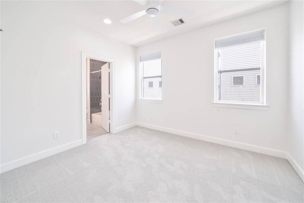 This bright bedroom features soft carpeting and two large windows, ensuring an abundance of natural sunlight fills the room.