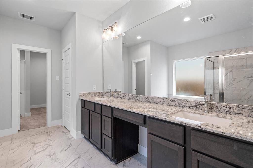 This primary bathroom is definitely move-in ready! Featuring stained wood cabinets with granite countertops, spacious walk-in closet with shelving, high ceilings, custom paint, sleek and dark modern finishes.