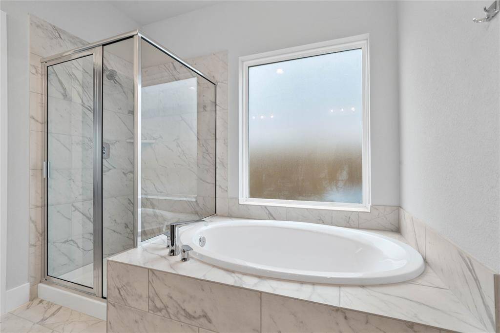 Additional view of this beautiful primary bathroom features a dark framed walk-in shower with tile surround, separate garden tub for soaking after a long day with custom tile detailing, high ceilings, custom paint, and a large tempered glass window for natural lighting.