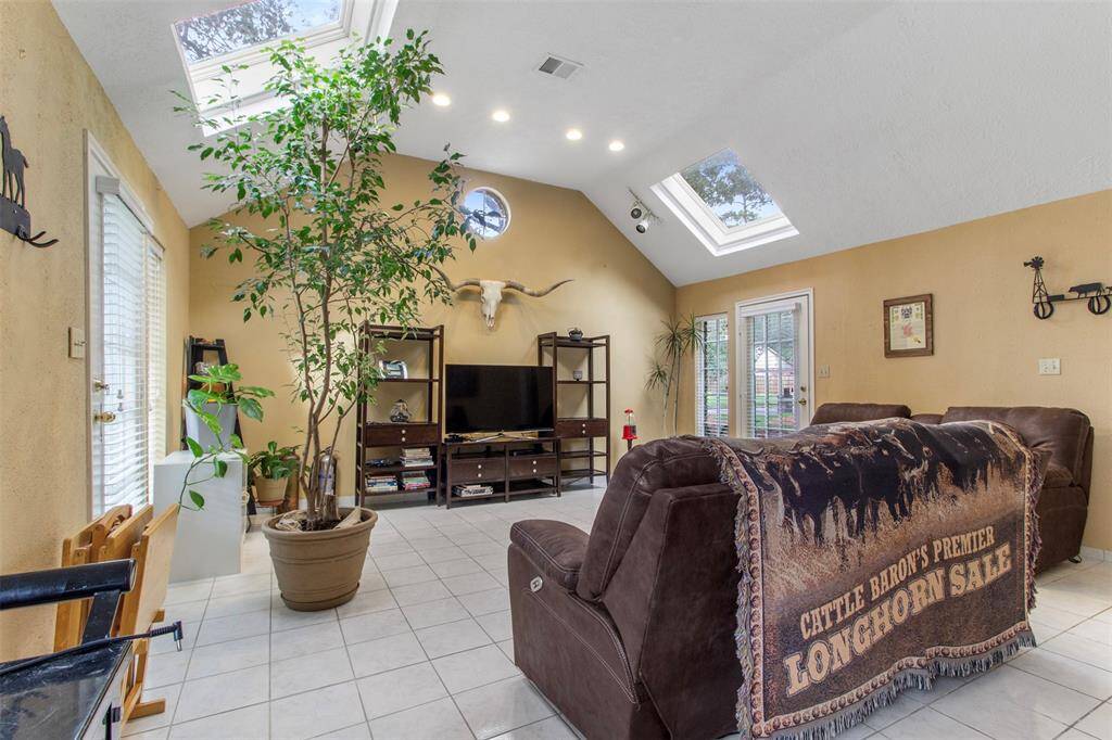 Living room features tile flooring, high ceilings, skylights, custom paint, and large windows.
