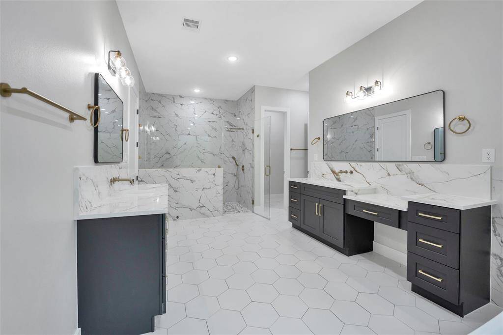 It includes a large soaking tub, a walk-in shower with modern fixtures, and dual vanities with sleek countertops