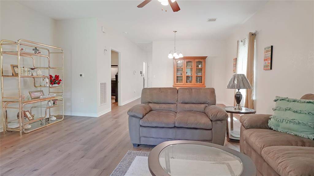 Bright and welcoming, this spacious living room features wood-look flooring, neutral tones, and an open layout perfect for relaxing or entertaining. Natural light and cozy seating make it feel like home.