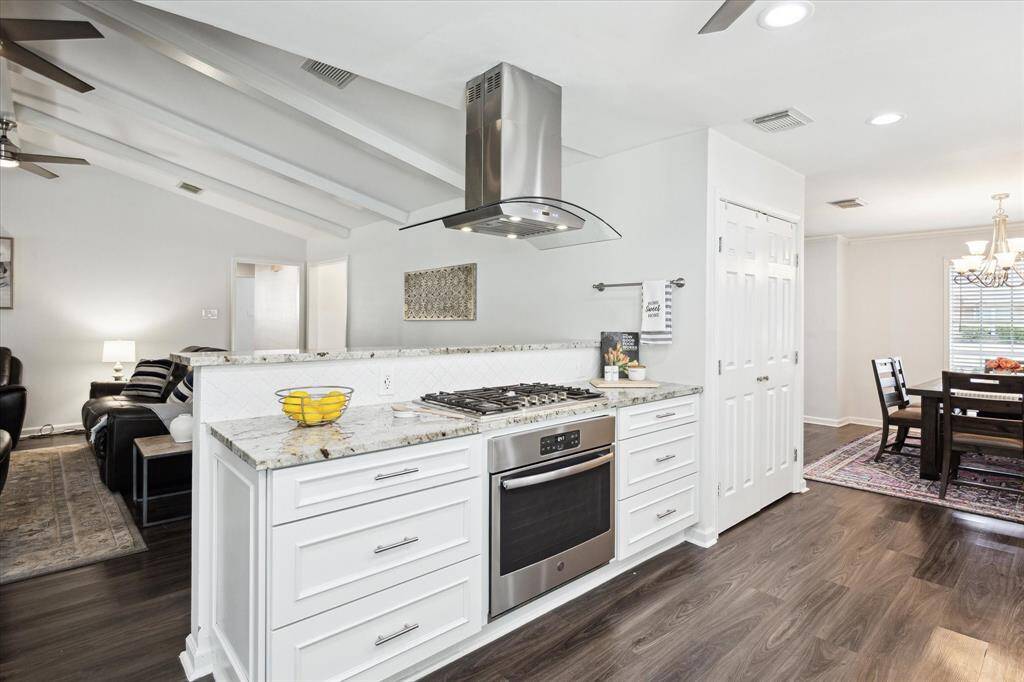This view from the kitchen showcases the gas range with stainless steel hood, granite countertops, and abundant storage—all while keeping you connected to the family room.
