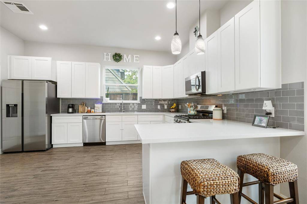 This modern kitchen features crisp white cabinetry, stainless steel appliances, and a sleek gray tile backsplash, all brought to life by generous natural light. The spacious layout invites effortless cooking and conversation, making it a central hub for daily routines and weekend gatherings alike.