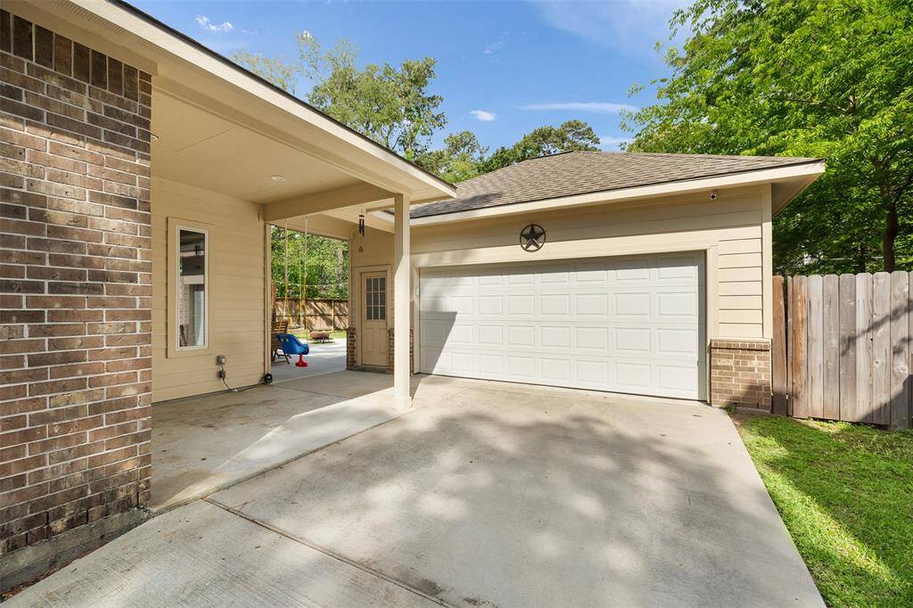 The spacious driveway leads to a two-car garage with a charming decorative touch, all set against a well-maintained brick and siding exterior. A covered entryway adds to the home’s curb appeal, while the surrounding greenery and wooden fence offer a sense of privacy and a peaceful outdoor setting.