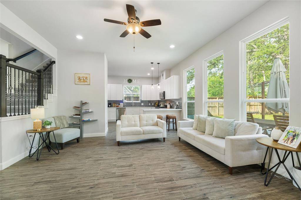 This spacious open-concept living area is filled with natural light from large windows and showcases beautiful wood flooring, a modern ceiling fan, and effortless flow into the kitchen. With its clean lines and welcoming layout, it’s a space where everyday living and entertaining come together with ease.