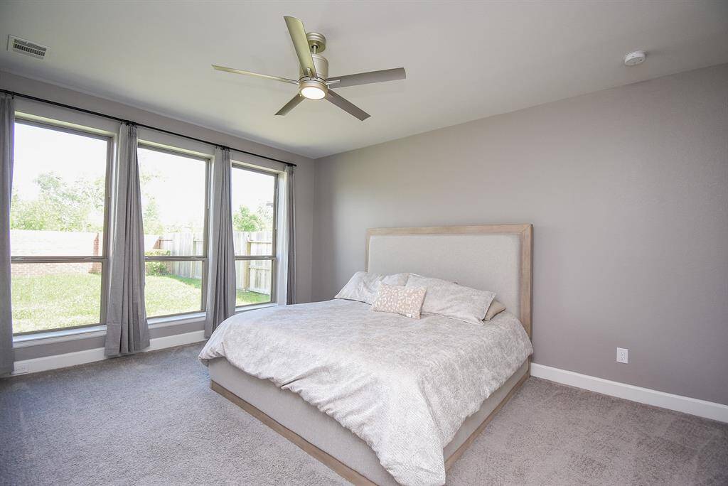 Primary Suite with a pewter ceiling fan, Floor-to-ceiling windows to welcome the morning! Plush carpet, and soft grey paint color for easy decorating.