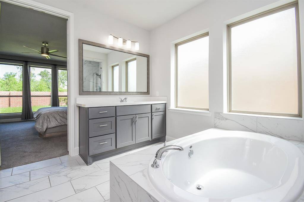 Luxurious master bath with oversized soaking tub, large wood framed mirrors, white and grey stone floors and lots of natural light.