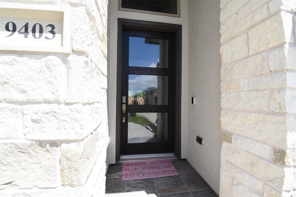 Clean White stone front porch with a Modern wood/glass door.