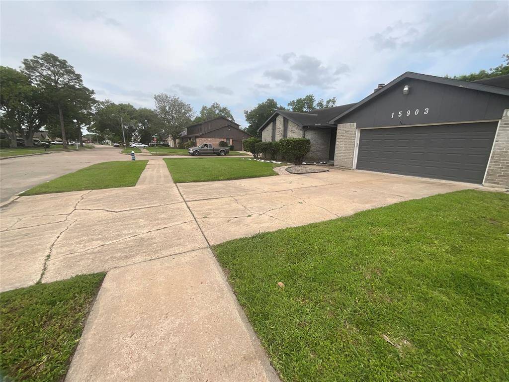 This photo shows a single-story home with a two-car garage, located on a corner lot. The exterior is modern with a dark color scheme. The driveway and sidewalk are spacious, and there's a well-maintained lawn. The neighborhood appears quiet and residential.