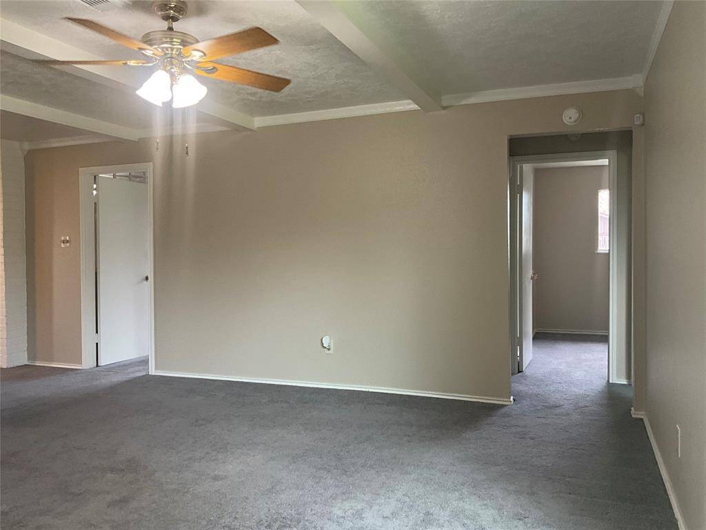 Spacious living room with neutral tones, featuring a ceiling fan and plush carpet, offering a cozy and inviting atmosphere.