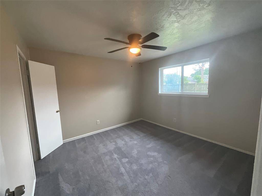 Cozy second bedroom featuring a large window for natural light, soft carpet, and a modern ceiling fan. Perfect for guests or a home office.