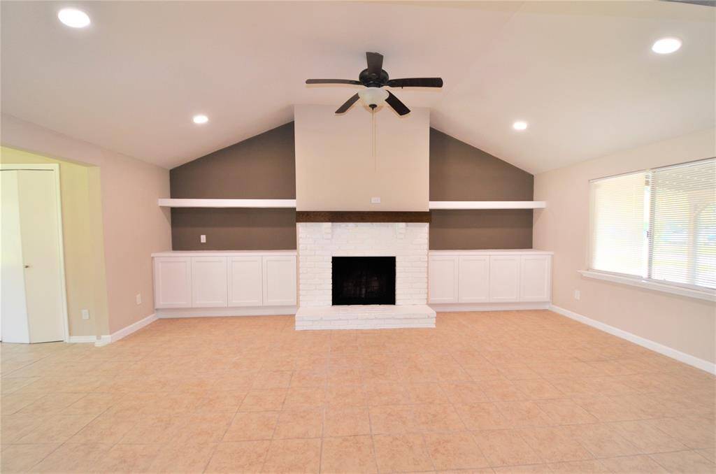 Spacious vaulted living room with built-in cabinets, sleek gas log fireplace, ceiling fan and great LED lighting.